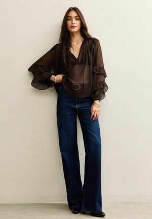 Svart genomskinlig blus med volangärmar, matchad med högmidjade utsvängda mörka jeans. Outfiten är accessoriserad med armband och ett bälte.