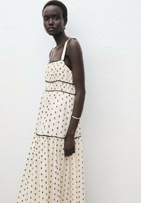 Vestido maxi blanco con acentos y ribetes de patrón negro, con tirantes finos y un corte relajado, hecho de tejido ligero.