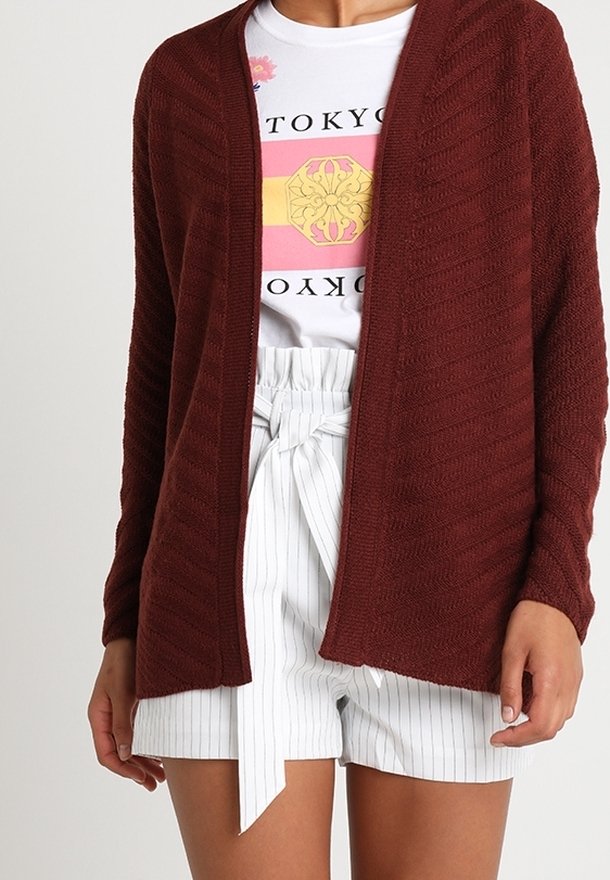 Femme portant un cardigan bordeaux ouvert sur un tee-shirt blanc avec un motif Tokyo et un short blanc à rayures taille haute avec une ceinture nouée.