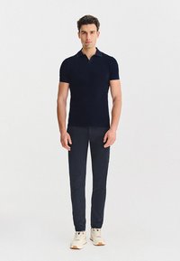 Granatowa koszulka polo z krótkim rękawem, klasycznym kołnierzykiem, zestawiona z ciemnymi spodniami i białymi trampkami z kolorowymi akcentami.