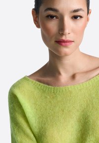 Világoszöld, áttetsző kötött pulóver széles nyakkivágással, puha tapintású és laza szabású, enyhe árnyalatváltással és bordázott szegélyekkel.