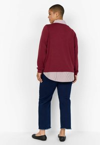 Parte superior de manga larga color burdeos con un cuello a rayas, combinada con unos jeans azul oscuro. Unos zapatos negros texturizados tipo slip-on completan el conjunto.