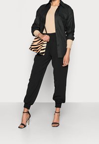 Černá košilová košile, béžový žebrovaný top, černé dámské tepláky s elastickými manžetami, černé sandály na vysokém podpatku s pásky a kabelka se zebřím vzorem.