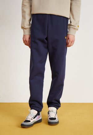 Navy sweatpants with elastic cuffs, paired with black and pastel-colored sneakers. Smooth texture with a relaxed fit design.