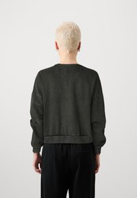 Sudadera corta en gris oscuro, con puños anchos y cuello redondeado. Textura suave con sutiles detalles de costura en las costuras.