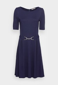 Mörkblå klänning med korta ärmar, figurnära liv, utsvängd kjol och en silverfärgad dekorativ bältesdetalj i midjan. Slät tygtextur.