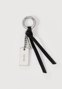 Μπρελόκ από μέταλλο Calvin Klein με ορθογώνιες πλακέτες και δύο μαύρα δερμάτινα λουριά σε λευκό φόντο.