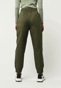 Groene, gestructureerde joggerbroeken met een elastische tailleband en taps toelopende manchetten, gecombineerd met zwart-witte sneakers.