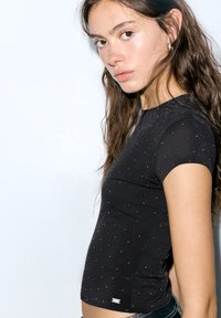 Top negru cu mâneci scurte, cu un design mulat, featuring mici decoruri argintii și un decolteu rotund. Material moale și elastic.