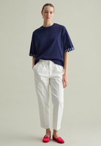 Camiseta oversized azul marino con puños a rayas, combinada con pantalones blancos ajustados y zapatos planos rojos, con un fondo neutro.
