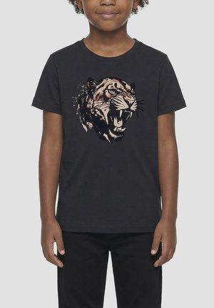 Enfant portant un t-shirt noir avec un motif de tête de tigre rugissante sur le devant, associé à un pantalon noir sur un fond uni.
