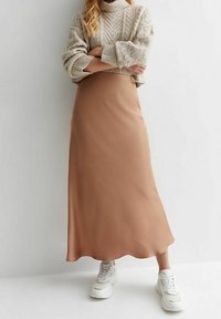 Maxikjol i mjuk tan-färgad tyg med en slät textur, kombinerad med en tjock krämfärgad stickad tröja och vita sneakers. Enkel, elegant design.