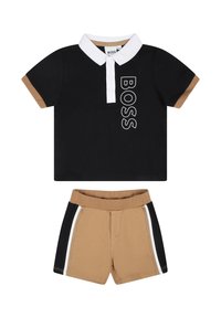 Polo noir avec un col blanc et le logo "BOSS", associé à un short beige avec des rayures latérales noires et blanches. Matière en coton.