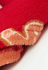 Červená a oranžová fleece deka s plyšovou texturou. Okraje mají zahnutý, kontrastní oranžový design s huňatými detaily.
