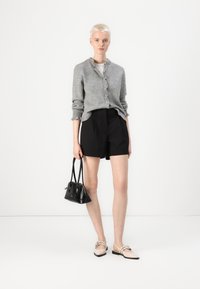 Grå ull knapp-opp cardigan, svarte skreddersydde shorts, lyse flate sko med sløyfe og en liten svart håndveske. Minimalistisk design.