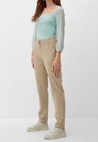 Ljusblå topp med fyrkantig halsringning och halvgenomskinliga puffärmar, kombinerad med beiga smala byxor och ljusa sneakers, som har knappdetaljer.