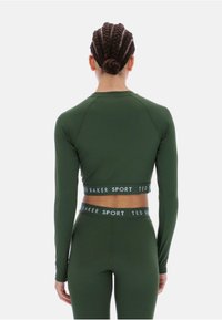 Tamsiai žalia ilgarankovė sportinė palaidinė, pagaminta iš tamprios medžiagos. Klostytas dizainas su "TED BAKER SPORT" logotipu ant juosmens.