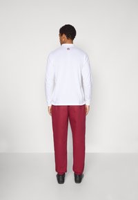 Balta ar garām piedurknēm krekls ar apaļu kakla izgriezumu, aizmugurē sarkans logs, saskaņots ar burgundijas krāsas biksēm un melnām kurpēm. Vienkāršs dizains ar brīvu piegriezumu.