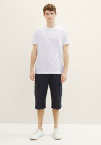 Weißes T-Shirt mit kurzen Ärmeln, kombiniert mit navyblauen Cargo-Shorts mit Seitentaschen und geradem Schnitt, getragen mit weißen Sneakern.