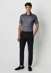 Kurzärmliges Hemd mit Knopfleiste aus dunkelgrauem Stoff mit subtiler Textur, kombiniert mit dunklen Hosen und schwarzen Slippern.