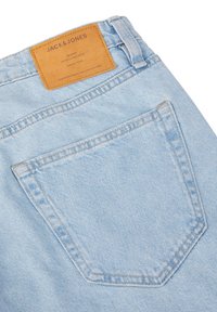 Jeans de mezclilla azul claro con un solo bolsillo trasero, que presenta una etiqueta de cuero marrón con texto en relieve en la cintura.