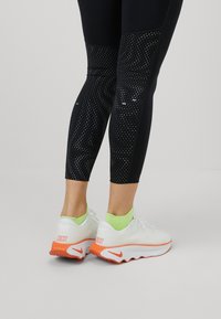 Sorte leggings med et prikket mønster og solide sektioner, parret med hvide sneakers med orange accenter og neongrønne sokker.