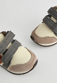 Tan en crème kindersneakers met grijze klittenbandsluitingen, gedetailleerd mesh bovenwerk en bruine rubberen zolen. Ronde neus en versterkte accenten.