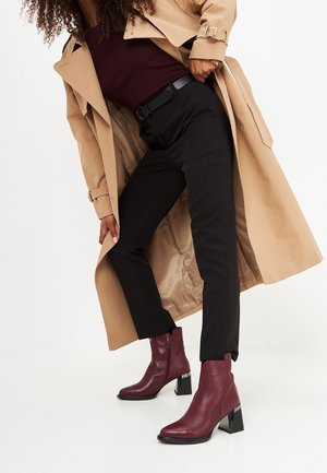 Bordeauxfarvede læderankelstøvler med firkantet tå, lynlåslukning og en blank sort blokhæl. Bruges med sorte bukser og en tanfarvet trenchcoat.