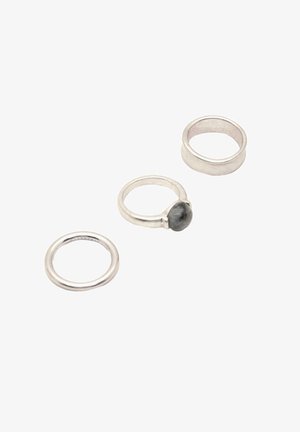 Tre anelli d'argento sono disposti: un semplice cerchio, un anello di tipo testurizzato e un anello con una pietra scura incastonata in un sottile band.