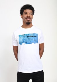 Hvid bomulds t-shirt med et blåt abstrakt kortdesign med sorte konturer; korte ærmer og en rund halsudskæring.