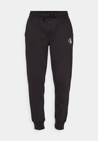 Schwarze, konisch zulaufende Jogginghosen mit elastischen Bündchen, Kordelzugbund, Seitentaschen und kleinem weißem CK-Logo am oberen linken Oberschenkel.