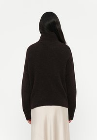 Mørkebrune genser med høy hals og avslappet passform, laget av mykt strikkemateriale. Sømløse skuldre og en litt cropped hem.