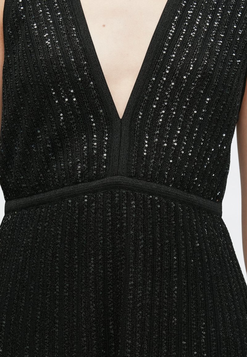 Black sequined dress with a deep V-neckline, featuring vertical ribbed texture and a fitted waistband. Accents contain shimmering sequins.