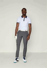 Balta polo krekls ar zilu apkakli, pelēkas piedurknēs veidotas bikses, balta josta un golfa nūja rokā. Apavi ir balti ar ziliem akcentiem.