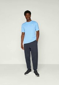 Lichtblauw sportshirt met korte mouwen, donkerblauwe trainingsbroek en zwarte sportschoenen, met een logo op het shirt en zijaccenten op de broek.