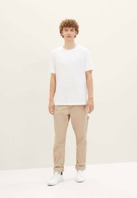 White short-sleeve t-shirt paired with beige chinos and white sneakers. Simple design with a relaxed fit, minimal texture, and no patterns.