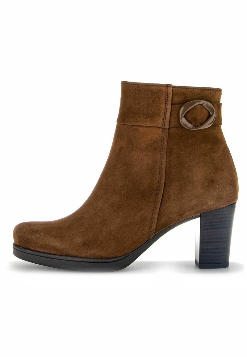 Bottine en suede marron avec un bout rond, un accent de boucle sur le côté et un talon épais noir. Texture lisse avec des détails de couture subtils.