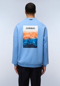 Felpa di colore blu chiaro con collo a giro, con una grafica rettangolare di montagne arancioni e blu sul retro. Polsini e orlo a costine.