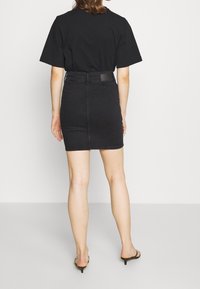 Zwarte katoenen T-shirt gecombineerd met een zwarte denim rok met hoge taille. De rok heeft een rechte snit en een eenvoudig ontwerp, geaccentueerd door een kleine zwarte riem.