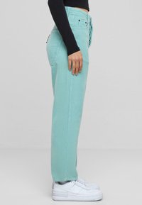 Pantaloni in corduroy turchese chiaro con vestibilità dritta, cinque tasche e una texture sottile, abbinati a sneaker bianche.