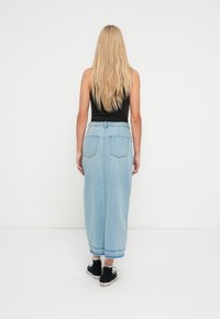 Lichtblauwe denim maxi-rok met een hoge taille en zichtbare achterzakken. Draagt zwarte sneakers en een aansluitende zwarte tanktop.