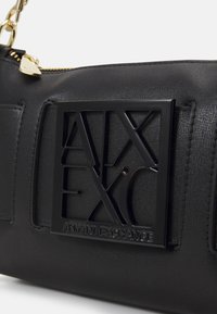 Must mustr nahkakott, millel on tõstetud must logo "Armani Exchange". Disain sisaldab lukuga sulgemist ja kuldset ahelat.