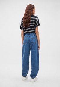 Ριγέ ασπρόμαυρο πλεκτό κοντό πουλόβερ, συνδυασμένο με φαρδιά μπλε τζιν παντελόνια υψηλής μέσης και λευκά αθλητικά παπούτσια.