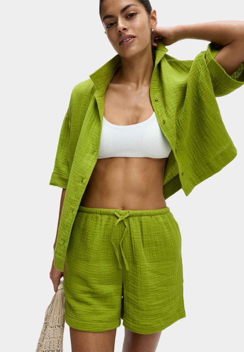 Felle groene, textured katoenen outfit met een knoopsluiting, korte mouwen en bijpassende shorts met trekkoord, aangevuld met een witte ribbed crop top.