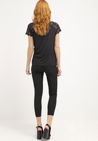 Czarna bluzka z koronkowymi rękawami, zestawiona z czarnymi legginsami. Strój charakteryzuje się gładką teksturą i dopasowanym krojem, dopełniony szpilkami.