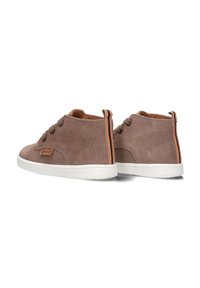 Braune Wildleder-Ankle-Boots mit weißen Gummisohlen, die braune Schnürsenkel, ein Markenetikett und einen mehrfarbigen gestreiften Akzent auf der Rückseite haben.