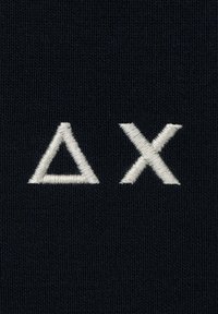 Tessuto navy strutturato con simboli geometrici bianchi ricamati: un triangolo (Δ) e una "X". Ogni simbolo presenta una texture leggermente in rilievo.