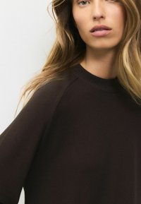 Suéter marrón con una textura suave, cuello de canalé y mangas raglán. La tela parece cálida y cómoda, adecuada para uso casual.