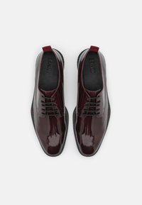 Chaussures habillées en cuir verni bordeaux avec un design à lacets, texture lisse, petit talon et fin contour noir le long de la semelle.