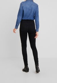 Jeans ajustados de cintura alta en negro con una textura suave, diseñados con bolsillos traseros y combinados con una camisa de mezclilla azul con detalles de botones.
